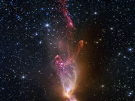 NASA Webb Reveals Stunning Details of Star Formation At the center is a thin vertical cloud known as Lynds 483 that is shaped like an hourglass with irregular edges. At lower center are two discrete bright white, tiny blobs of light that have raced away from the hidden central stars. The top lobe shows a more prominent orange U-shape. Orange bleeds into light purple, and brighter pink at its edges. Some background stars are visible through sections of this lobe. Higher up, there is an orange arc. Some brighter pink material extends to the top edges near the center. In the lower lobe, less orange is visible. More opaque light purple is in its top third, rippling out into semi-transparent blues and pinks. The lower lobe has more texture. V-shapes left and right of the lobes are darkest, and the background stars in these areas appear orange. Elsewhere, the black background of space is clearer, speckled with tiny white stars and faint orange galaxies.