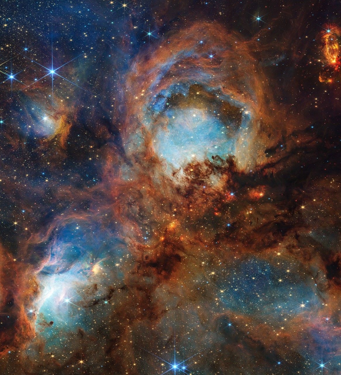 webb stsci 01jy2aza9gfmfrkwntg0hyb8kn 2k.jpg A section of the Cat’s Paw Nebula, a local star-forming region composed of gas, dust, and young stars. Four roughly circular areas are toward the center of the frame: a small oval toward the top left, a large circle in the top center, and two ovals at bottom left and right. Each circular area has a luminous blue glow, with the top center and bottom left areas the brightest. Brown-orange filaments of dust, which vary in density, surround these four bluish patches and stretch toward the frame’s edges. Small zones, such as to the left and right of the top-center blue circular area, appear darker and seemingly vacant of stars. Toward the center are small, fiery red clumps scattered among the brown dust. Many small, yellow-white stars are spread across the scene, some with eight-pointed diffraction spikes that are characteristic of Webb. A few larger blue-white stars with diffraction spikes are scattered throughout, mostly toward the top left and bottom right. In the top right corner is a bright red-orange oval.