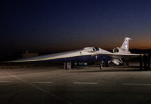 NASA Media Day for X-59 Test Flights Announced An aircraft resting on a section of runway as seen from the side. The X-59 has a long, thin nose that accounts for nearly a third of its length, along with sleek wings and an engine mounted above its body, just below its tail. The early morning sky is dark in the background with the sunrise just starting to emerge.