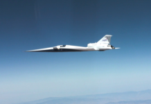 NASA Achieves Breakthrough in Supersonic Flight Technology NASA’s X-59 quiet supersonic research aircraft flies through the blue sky. The plane has a distinctive long, sharp nose. There are mountains visible at the bottom of the photo.