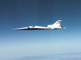 NASA Achieves Breakthrough in Supersonic Flight Technology NASA’s X-59 quiet supersonic research aircraft flies through the blue sky. The plane has a distinctive long, sharp nose. There are mountains visible at the bottom of the photo.